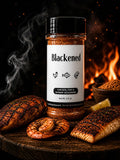 Blackened seasoning bottle with smoked chicken, fish, shrimp, and lemon slices against a fiery background.